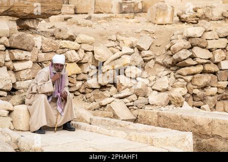 Un vieil homme local assis sur un rocher dans les pyramides de Gizeh en Égypte Banque D'Images