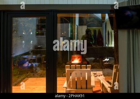 Un brazier avec feu et des charbons barbecue se tient la nuit près d'un chalet de vacances avec des portes en verre et des chaises en Altaï. Banque D'Images