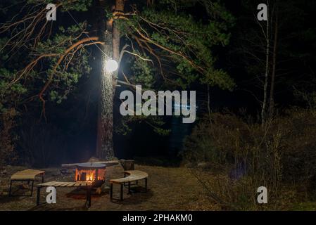 Un foyer, un foyer en métal entouré de bancs en bois se dresse la nuit sous un arbre avec une lanterne avec un feu sur les rives de la rivière Katun à Al Banque D'Images