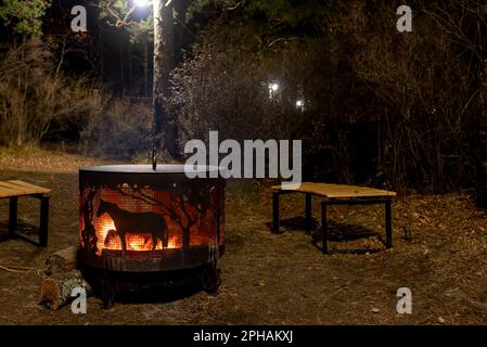 Un foyer, un foyer en métal, avec une silhouette de cheval, entouré de bancs en bois, se dresse la nuit sous un arbre avec une lanterne et un feu sur le Th Banque D'Images