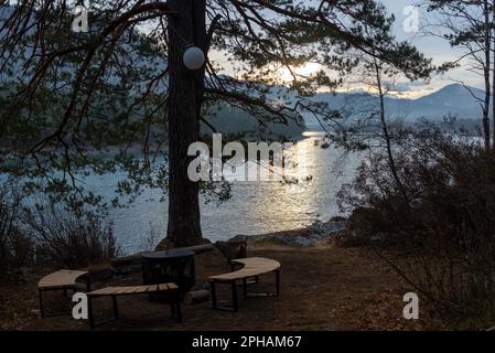 Un foyer, un foyer en métal entouré de bancs en bois se dresse à l'aube sous un arbre avec une lanterne sur la rive de la rivière Altai. Banque D'Images