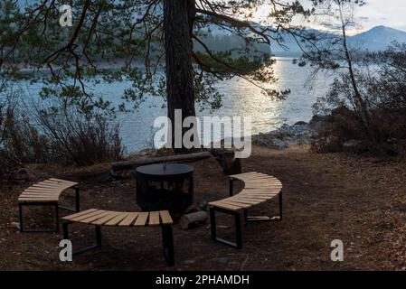 Un foyer, un foyer en métal entouré de bancs en bois, se dresse à l'aube sous un arbre avec une lanterne sur les rives de la rivière Katun en Altaï. Place FO Banque D'Images