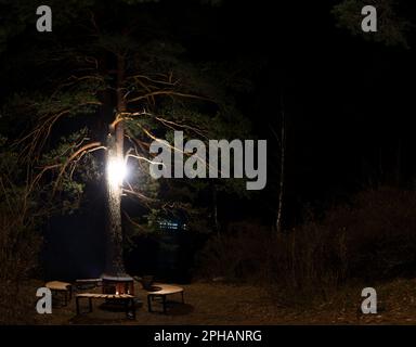 Un foyer, un foyer en métal entouré de bancs en bois, se dresse la nuit dans l'obscurité sous un arbre avec une lanterne avec un feu sur les rives du Katu Banque D'Images