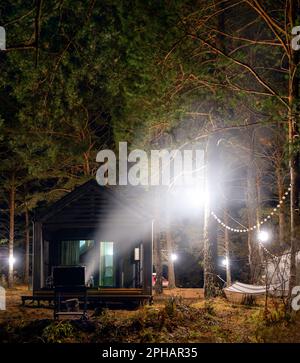 Un brazier avec feu et fumée et barbecue charcoals se tient la nuit près d'un chalet de vacances avec des portes en verre à Altai près d'une rivière et d'une forêt. Banque D'Images