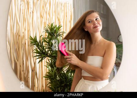 Une femme attirante peigne ses cheveux devant un miroir de salle de bains. Soins capillaires. Cosmétiques publicitaires pour soins capillaires. Banque D'Images