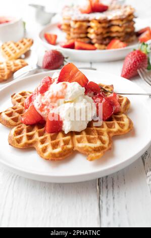 Gaufres avec sauce aux fraises et crème fouettée sur table blanche. Délicieux dessert pour la fête des mères Banque D'Images