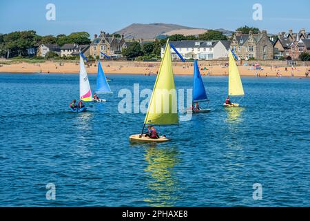 Les jeunes qui profitent du soleil d'été naviguent à bord d'un canot pneumatique dans le port d'Elie, avec la plage et la ville d'Elie en arrière-plan - Elie, Neuk est de Fife, Écosse, Royaume-Uni Banque D'Images