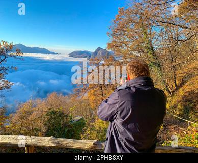 Photographe prenant des photos sur Mountain Peak San Salvatore au-dessus de Cloudscape avec lumière du soleil et ciel clair à Lugano, Tessin en Suisse. Banque D'Images