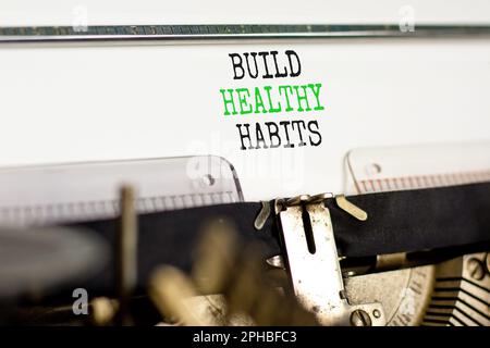 Symbole motivation construire des habitudes saines. Concept mots construire des habitudes saines sur papier blanc tapé sur vieux rétro machine à écrire sur beau fond blanc. Banque D'Images