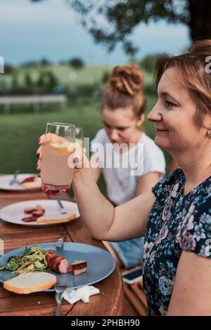 Famille ayant un repas du grill pendant le pique-nique d'été dîner en plein air dans un jardin de maison. Gros plan des personnes assises à une table avec de la nourriture et de la vaisselle Banque D'Images