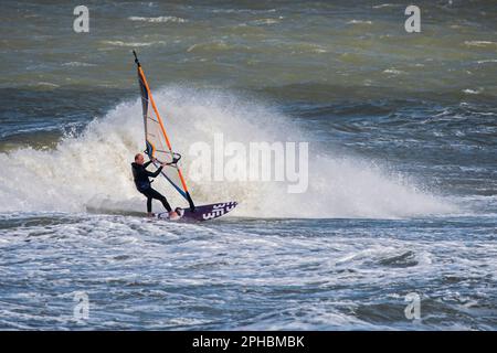 Planche à voile sportive en combinaison noire pratiquant la planche à voile classique le long de la côte de la mer du Nord par temps venteux pendant la tempête d'hiver Banque D'Images