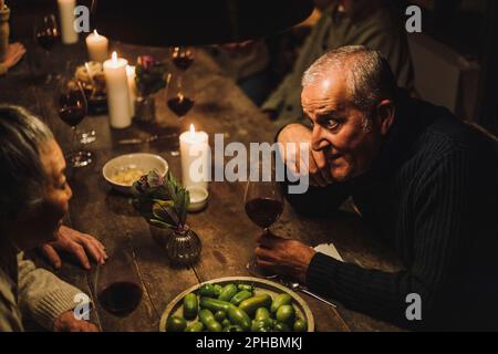 Vue en grand angle d'un homme mûr parlant avec une amie senior assise à la table de salle à manger pendant la fête Banque D'Images