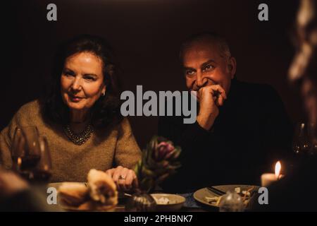 Homme mature avec main sur le menton par une amie femelle senior lors d'une soirée dîner Banque D'Images