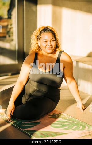 Jeune femme souriante assise sur un tapis d'exercice au centre de retraite Banque D'Images