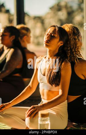 Des amies qui font de l'exercice tout en s'asseyant dos à dos en cours de yoga Banque D'Images