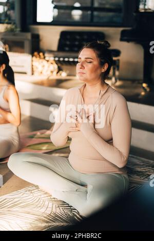 Femme méditant avec les mains sur la poitrine assis en travers des jambes au centre de retraite Banque D'Images