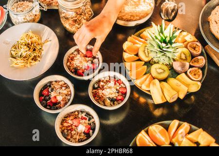 Main de la femme ramassant les baies du bol du petit déjeuner disposé sur une table Banque D'Images