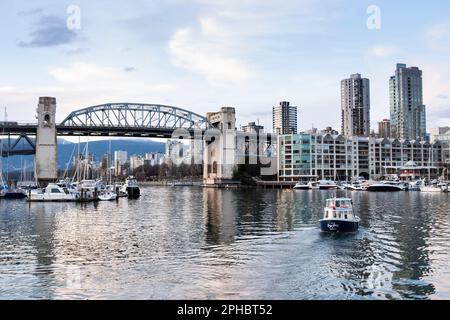 Un bateau-taxi aquabus part de Granville Island, avec le pont de Burrard Street et la ligne d'horizon de Vancouver au coucher du soleil au loin. Banque D'Images