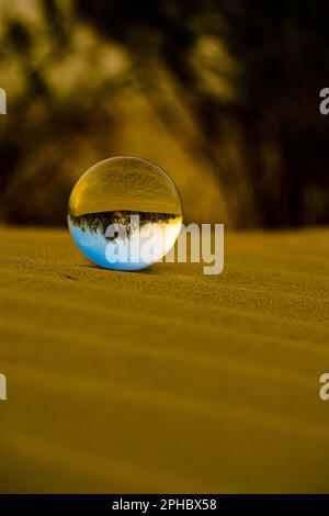 Une boule de verre reposant sur des sables dans un environnement naturel, avec des arbres flous en arrière-plan Banque D'Images