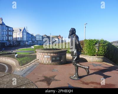 La statue d'Eric Morecambe (Eric Bartholomew. 1926–1984) de l'ancienne comédie due Morecambe et Wise. Il se trouve sur le front de mer à Morecambe, dans le Lancashire, au Royaume-Uni, au sommet d'un ensemble de marches gravées avec les mots de la paire signature Tune 'Bring Me Sunshine' gravés dans une police de type machine à écrire. Elle a été sculptée par Graham Ibbeson et dévoilée par feu la reine Elizabeth II en juillet 1999. Il se trouve non loin de la célèbre tour de 1905 horloge Tour de l'horloge. Conçu par Cressey et Keighley construit en brique rouge avec bandes et pansements de grès. Banque D'Images