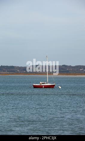 Un voilier rouge est ancré dans une baie, l'eau ne bouge pas, la bouée blanche devant la cale en place. Banque D'Images