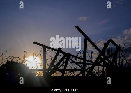 Silhouette de clôture barbelée avec le soleil brillant Banque D'Images