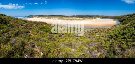 Panorama ultra grand angle de la rivière Ribeira de Aljezur qui serpente à travers le sable doré de la plage de Praia da Amoreira avec une eau calme et limpide. Banque D'Images