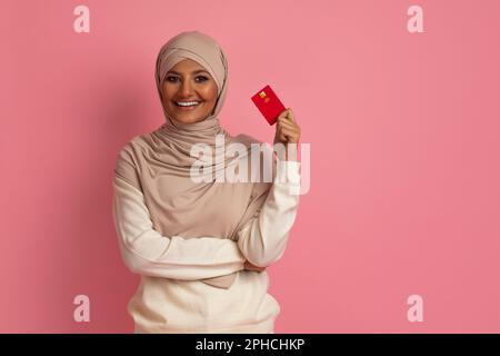 Belle femme musulmane dans hijab tenant la carte de crédit et souriant à la caméra Banque D'Images