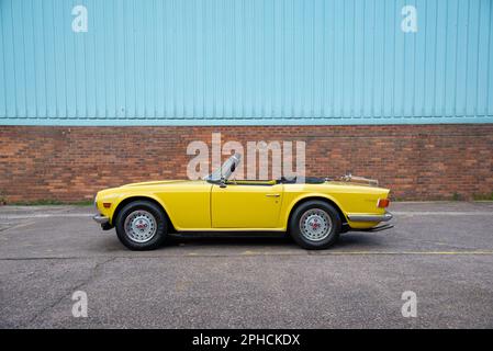 Triumph jaune TR6 stationné sur béton à côté d'un mur de briques Banque D'Images