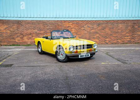 Triumph jaune TR6 stationné sur béton à côté d'un mur de briques Banque D'Images