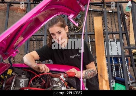Jeune femme mécanicien effectuant l'entretien sur un Austin Mini classique rose vif Banque D'Images