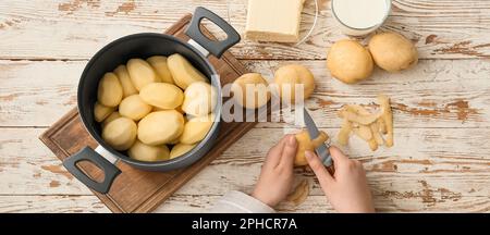 Femme épluchant des pommes de terre crues sur une table en bois blanc, vue de dessus Banque D'Images