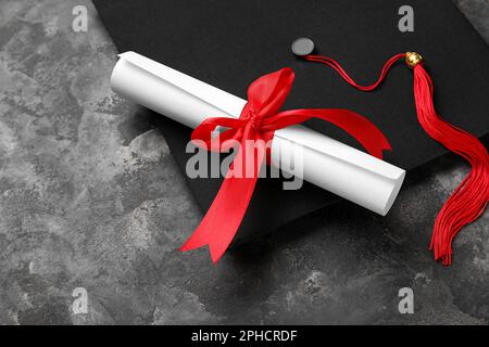 Diplôme avec ruban rouge et chapeau de graduation sur table gris foncé Banque D'Images