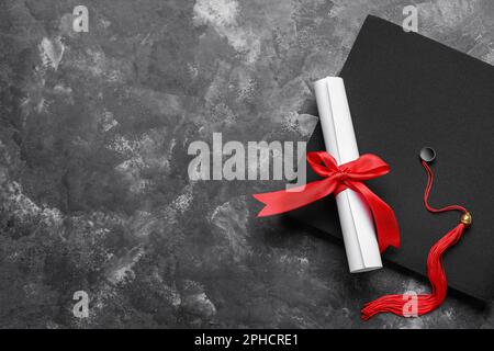 Diplôme avec ruban rouge et chapeau de graduation sur table gris foncé Banque D'Images