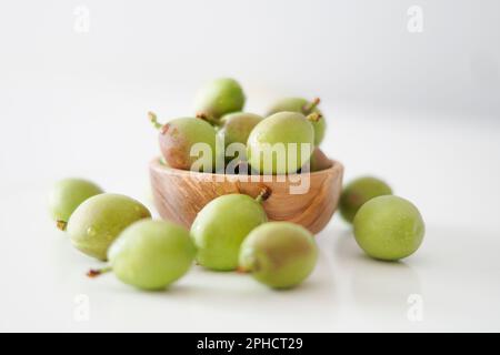 Un bol de pêches fraîches et non mûres sur fond blanc. Pêche verte fraîche brute dans un bol en bois. Banque D'Images