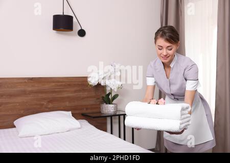 Belle femme de chambre mettant des serviettes propres sur le lit dans la chambre d'hôtel Banque D'Images