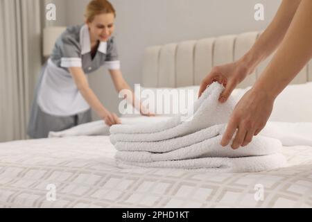 Femme de chambre mettant des serviettes propres sur le lit dans l'hôtel, à proximité Banque D'Images