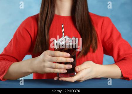 Femme tenant un verre de cola avec de la glace et de la paille à table bleue, gros plan. Soda rafraîchissante Banque D'Images