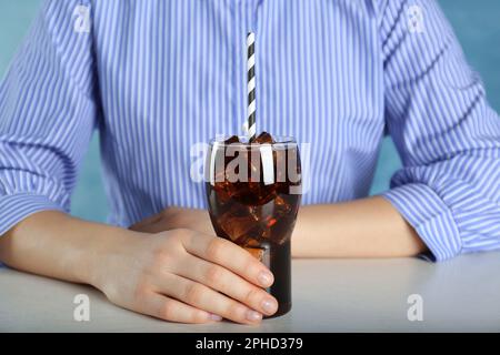 Femme tenant un verre de cola avec de la glace et de la paille à la table blanche sur fond bleu clair, gros plan. Soda rafraîchissante Banque D'Images