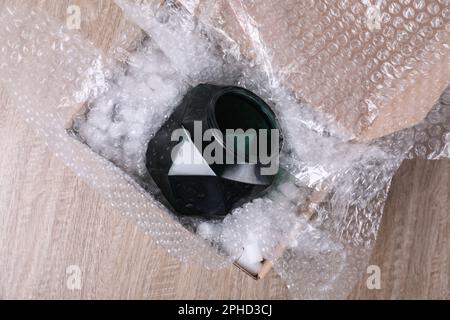 Vase en verre avec film à bulles et mousse d'emballage dans une boîte en carton sur une table en bois, vue de dessus Banque D'Images