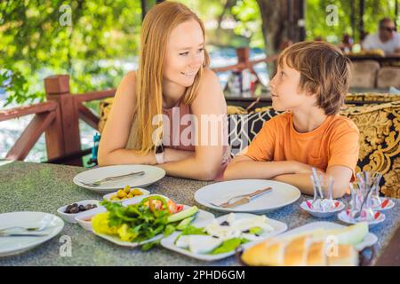 Maman et son prennent un petit déjeuner turc. Table de petit-déjeuner turc. Pâtisseries, légumes, légumes verts, olives, fromages, œufs frits, épices, confitures, miel, thé Banque D'Images