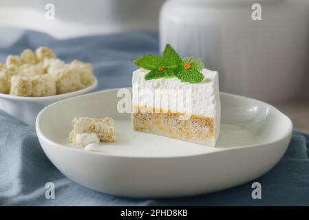 Gâteau à la mousse blanche décoré de feuilles de menthe sur une assiette sur une nappe grise Banque D'Images