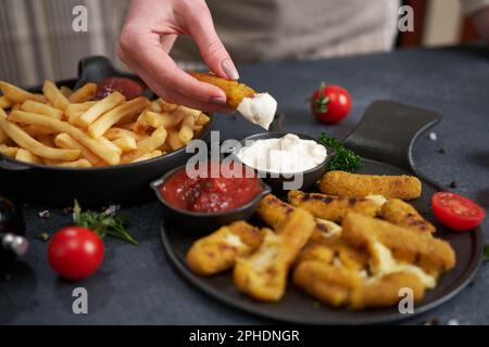 La femme trempette le bâton de mozzarella au fromage dans la sauce trempée Banque D'Images