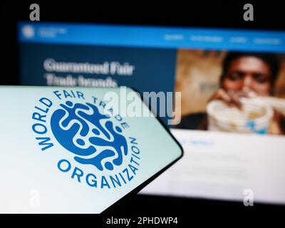 Smartphone avec le logo de l'Organisation mondiale du commerce équitable (WFTO) à l'écran devant le site Web. Mise au point au centre-gauche de l'écran du téléphone. Banque D'Images