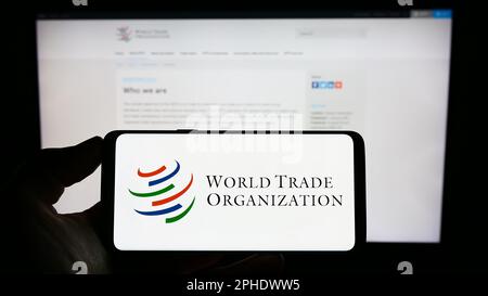 Personne tenant un téléphone portable avec le logo de l'Organisation mondiale du commerce (OMC) à l'écran devant la page Web. Mise au point sur l'affichage du téléphone. Banque D'Images