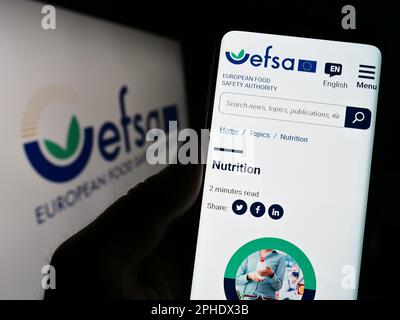 Personne tenant un téléphone portable avec une page web de l'Agence européenne de sécurité des aliments (EFSA) à l'écran avec logo. Concentrez-vous sur le centre de l'écran du téléphone. Banque D'Images