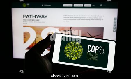 Personne tenant un smartphone avec le logo de la Conférence des Nations Unies sur le changement climatique COP28 (Dubaï) à l'écran devant le site Web. Mise au point sur l'affichage du téléphone. Banque D'Images