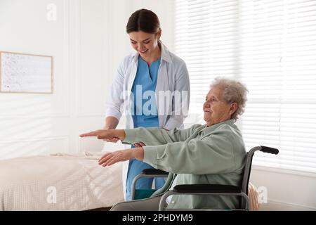 Femme âgée en fauteuil roulant faisant de l'exercice physique à l'intérieur. Service de soins de santé à domicile Banque D'Images