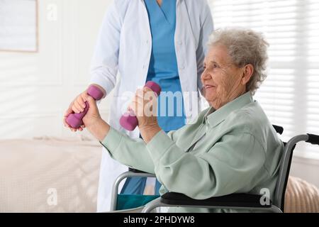 Femme âgée en fauteuil roulant faisant de l'exercice physique à l'intérieur. Service de soins de santé à domicile Banque D'Images