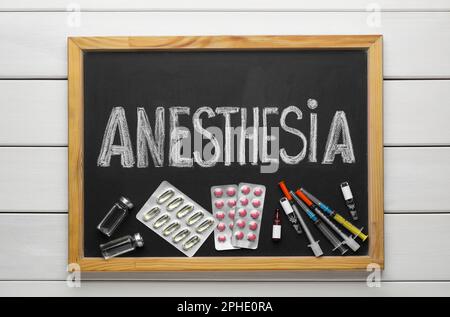 Tableau noir avec anesthésie par mot, seringues et médicaments sur table en bois blanc, vue de dessus Banque D'Images
